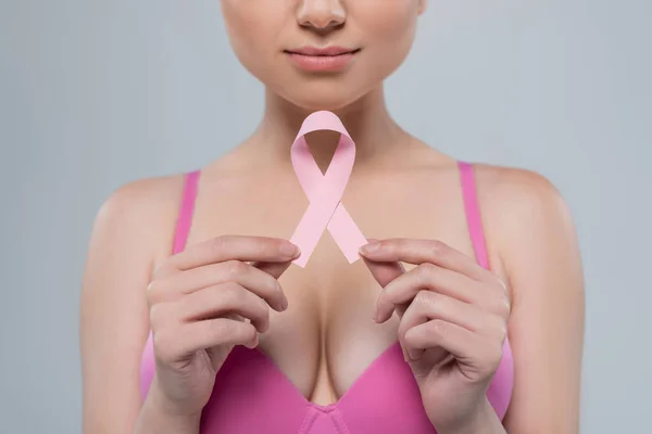 Partial view of woman in pink bra holding breast cancer awareness ribbon isolated on grey — Stock Photo