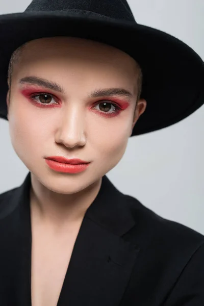 Retrato de jovem com maquiagem vermelha carmim, vestindo chapéu fedora preto isolado em cinza — Fotografia de Stock