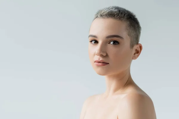 Mujer joven con piel perfecta, maquillaje natural y hombros desnudos mirando a la cámara aislada en gris - foto de stock