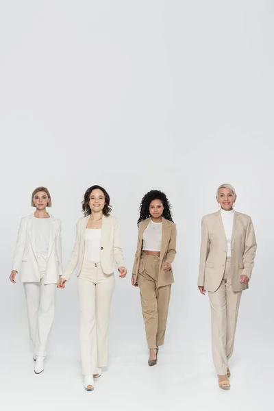 Full length of multiethnic businesswomen walking on grey background, feminism concept — Stock Photo