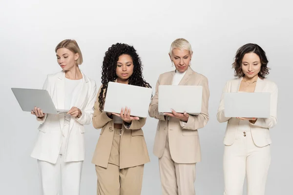 Empresarias multiétnicas usando computadoras portátiles aisladas en gris, concepto feminista - foto de stock