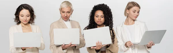 Interrassische Geschäftsfrauen in formeller Kleidung mit Laptops auf grauem Banner — Stockfoto