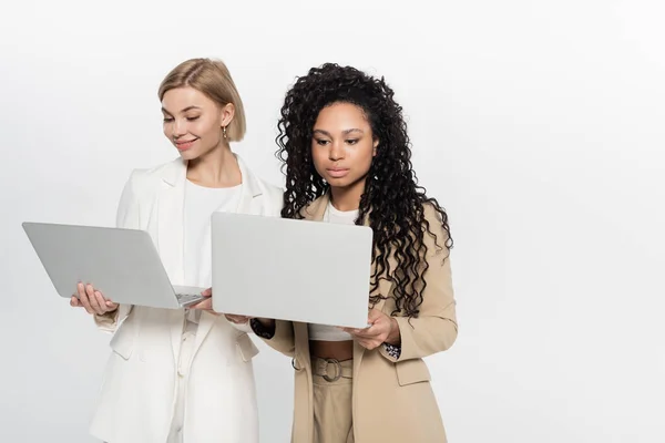 Young multiethnic businesswomen using laptops isolated on grey — Stock Photo