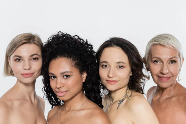 Positive interracial women with naked shoulders looking at camera isolated on grey — Stock Photo