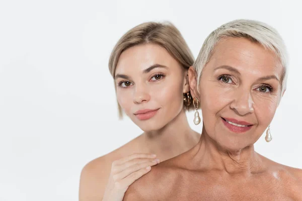 Young woman touching naked shoulder of senior friend isolated on grey — Stock Photo