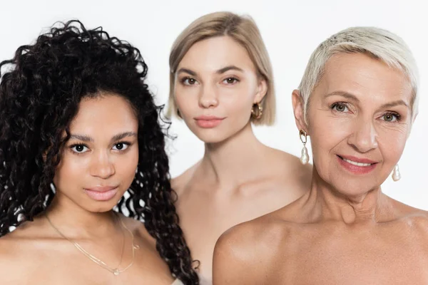 Interracial women with naked shoulders looking at camera near blurred friend isolated on grey — Stock Photo