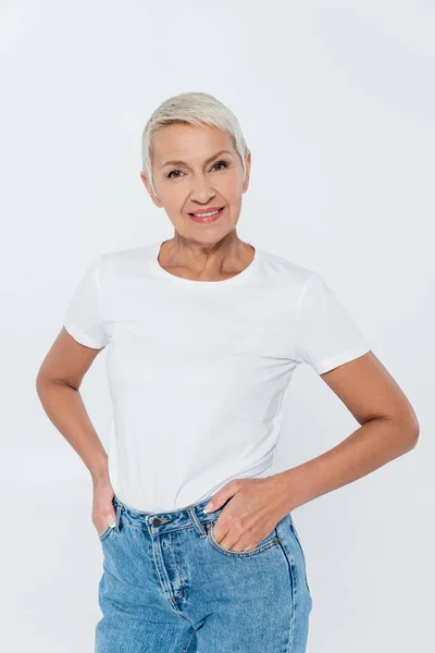 Позитивная пожилая женщина в футболке и джинсах позирует изолированно на серой — стоковое фото