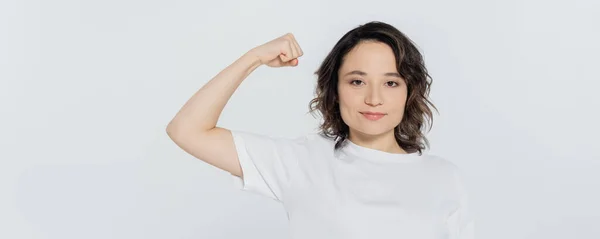 Brunette woman showing muscles and looking at camera isolated on grey, banner — Stock Photo