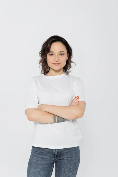 Sonriente mujer tatuada cruzando brazos aislados en gris - foto de stock