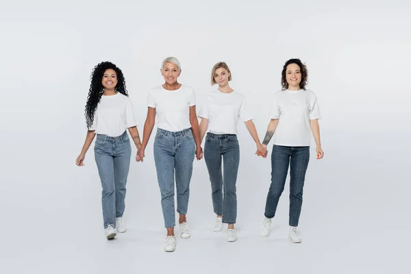 Full length of interracial women holding hands on grey background — Stock Photo