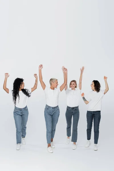 Mulheres multiétnicas positivas levantando as mãos sobre fundo cinza, conceito de feminismo — Fotografia de Stock