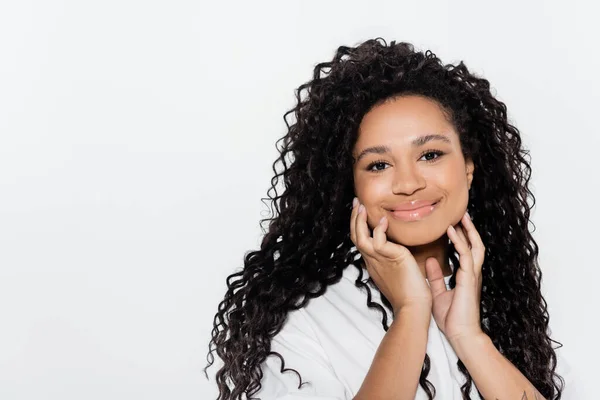 Mujer afroamericana positiva tocando la cara aislada en gris - foto de stock