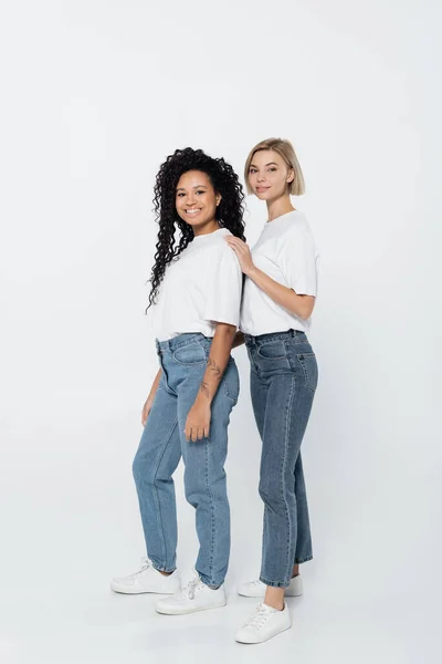 Longitud completa de la mujer sonriente abrazando amigo afroamericano sobre fondo gris - foto de stock