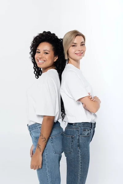 Smiling interracial women standing back to back isolated on grey — Stock Photo