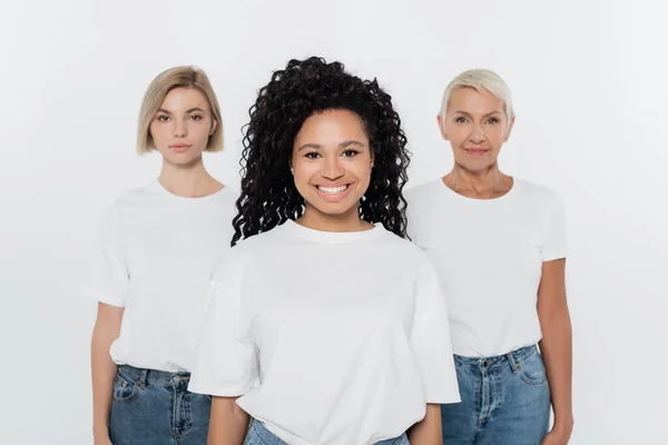 Sonriente mujer afroamericana mirando a la cámara cerca de amigos borrosos aislados en gris - foto de stock