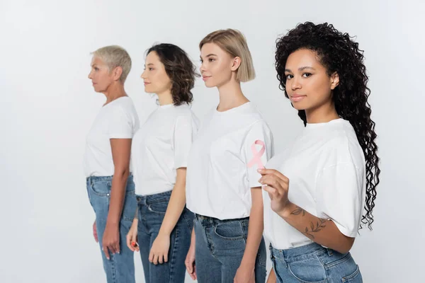 African american woman holding pink ribbon of breast cancer awareness near friends isolated on grey — Stock Photo