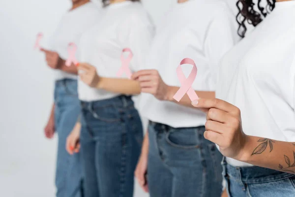 Vista recortada de la mujer afroamericana sosteniendo cinta de conciencia de cáncer de mama cerca de amigos borrosos aislados en gris - foto de stock