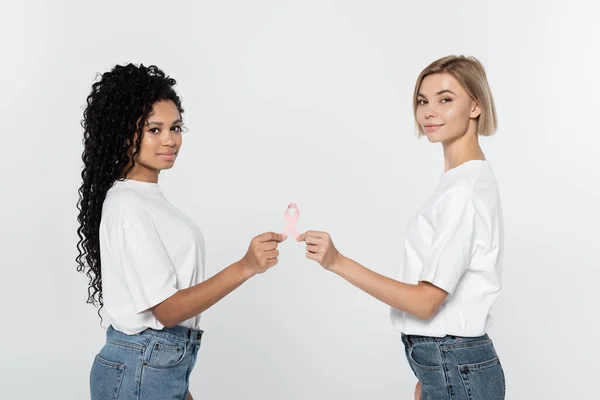 Mujeres jóvenes interracial sosteniendo cinta rosa de conciencia de cáncer de mama aislado en gris - foto de stock