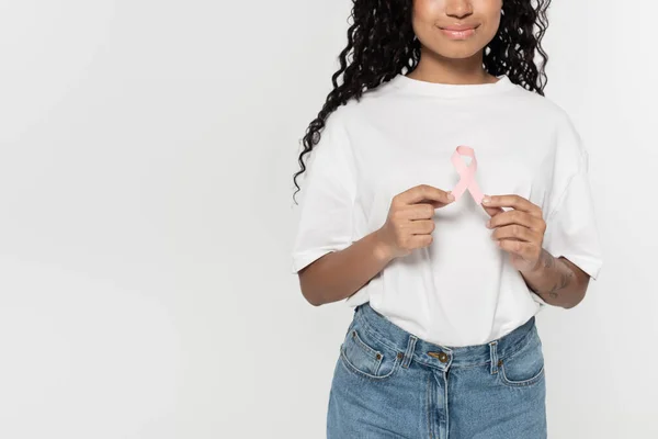 Vista recortada de una joven afroamericana sosteniendo cinta rosa de conciencia de cáncer de mama aislada en gris - foto de stock