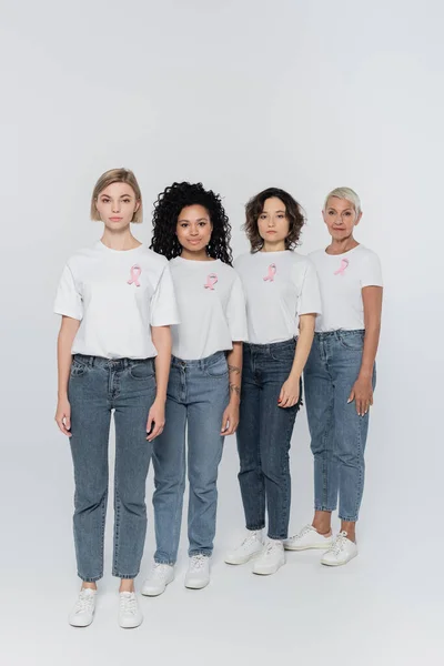 Interracial women with pink ribbons on t-shirts looking at camera on grey background — Stock Photo