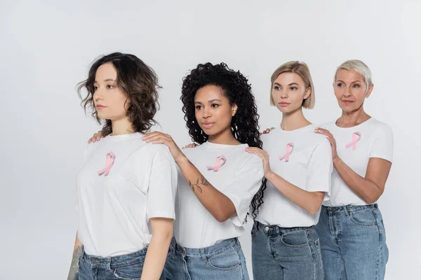 Multiethnic women with ribbons of breast cancer awareness looking away isolated on grey — Stock Photo