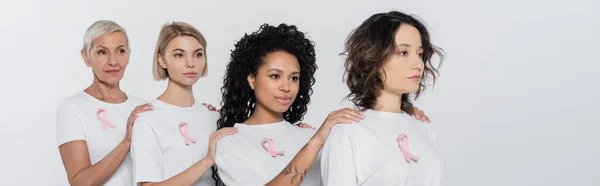 Interrassische Frauen mit Bändern des Brustkrebsbewusstseins stehen isoliert auf grauem Banner — Stockfoto