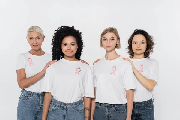 Femmes avec des rubans roses sur des t-shirts touchant des amis interracial isolés sur gris — Photo de stock