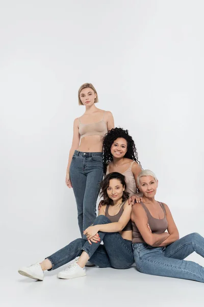 Happy multiethnic women posing while sitting on grey background — Stock Photo