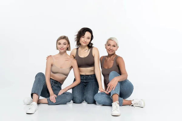 Women in tops and jeans looking at camera on grey background — Stock Photo