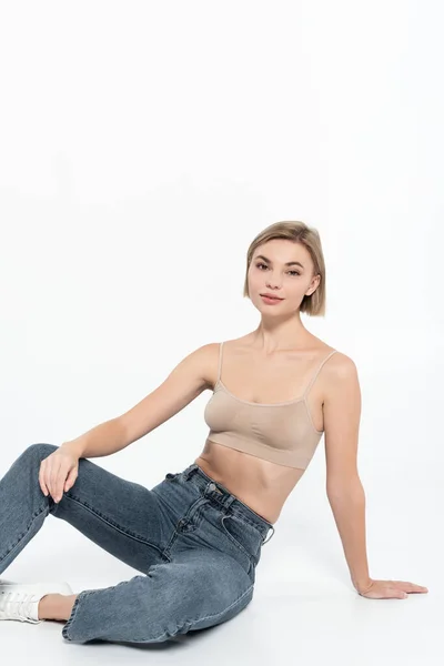 Young blonde woman in jeans posing on grey background — Stock Photo