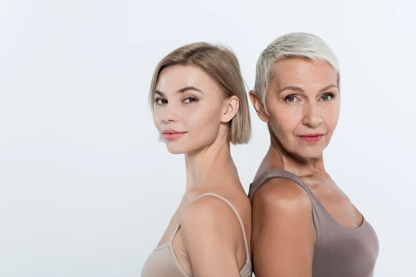 Mujeres mirando a la cámara mientras están de pie espalda con espalda aisladas en gris - foto de stock