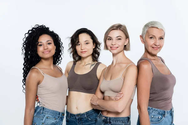 Positive interrassische Frauen in Tops, die auf grauem, feministischem Konzept isoliert in die Kamera schauen — Stockfoto