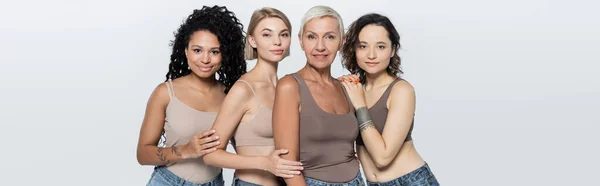 Interrassische Frauen umarmen und lächeln isoliert auf grauem Banner — Stockfoto