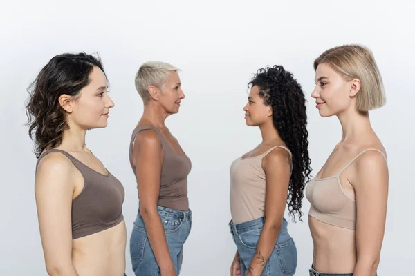 Vista lateral de mujeres multiétnicas mirándose aisladas en gris - foto de stock