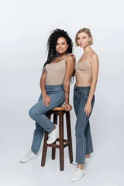 Femme afro-américaine assise sur une chaise près d'un ami sur fond gris — Photo de stock