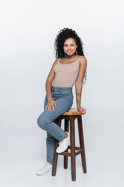 Mujer afroamericana feliz posando cerca de la silla sobre fondo gris - foto de stock