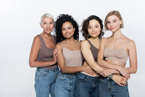 Glückliche interrassische Frauen, die sich umarmen und die Kamera isoliert auf grau anschauen — Stockfoto