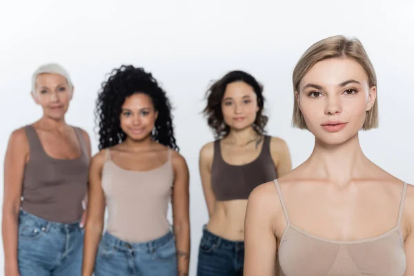 Blonde woman looking at camera near blurred interracial friends isolated on grey — Stock Photo