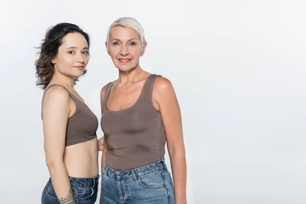 Brunette woman hugging cheerful elderly friend isolated on grey, feminism concept — Stock Photo