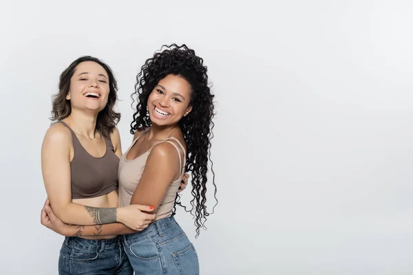 Femme afro-américaine bouclée embrassant amie gaie isolé sur gris, concept féminisme — Photo de stock