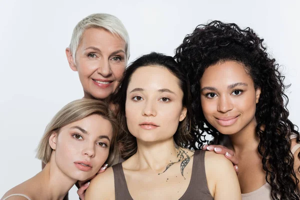 Lächelnde interrassische Frauen umarmen tätowierten Freund isoliert auf grau, Feminismus-Konzept — Stockfoto