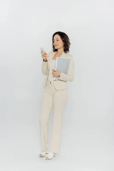 Businesswoman holding paper folder and using smartphone on grey background — Stock Photo