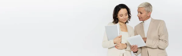 Деловая женщина держит цифровой планшет рядом с коллегой с бумажной папкой, изолированной на сером, баннер — стоковое фото