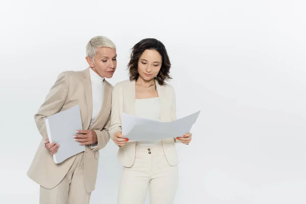 Jeune femme d'affaires tenant dossier papier près d'un collègue aîné isolé sur gris — Photo de stock