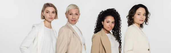 Multiethnic businesswomen in formal wear looking at camera isolated on grey, banner — Stock Photo