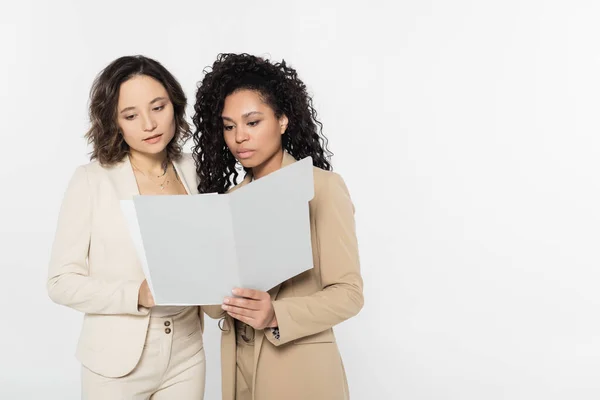 Empresarias multiétnicas mirando la carpeta de papel aislada en gris, concepto feminista - foto de stock