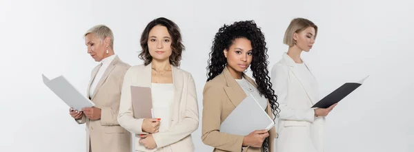 Multiethnische Geschäftsfrauen mit Papiermappen in der Nähe von Kollegen isoliert auf grauem Banner — Stockfoto