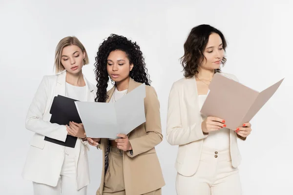 Міжрасові бізнес-леді тримають паперові папки поблизу колеги ізольовані на сірому — стокове фото