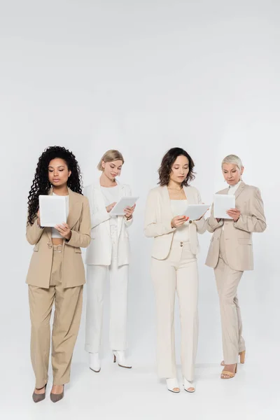 Empresarias interraciales usando tabletas digitales sobre fondo gris - foto de stock
