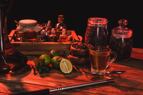 Limas frescas, té y narguile en superficie de madera aislada en negro - foto de stock